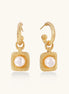 Pair of gold vermeil hoop earrings with textured square frames holding freshwater pearls on cream background