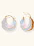 Shell-shaped hoop earrings with iridescent blue-pink enamel and gold trim on cream background