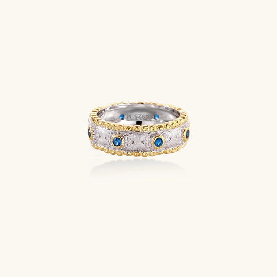 Two-tone ring with brushed silver center, gold beaded edges, and blue zirconia stones on white background.