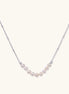 Delicate sterling silver chain necklace with small freshwater pearls arranged in a curved smile arc on cream background.