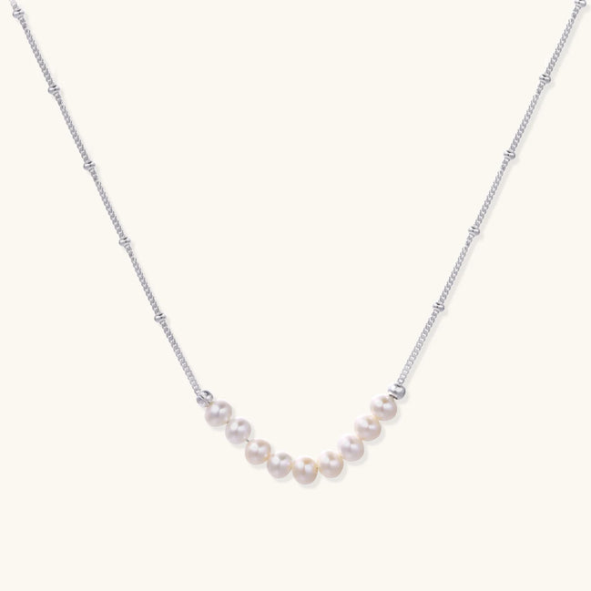 Delicate sterling silver chain necklace with small freshwater pearls arranged in a curved smile arc on cream background.